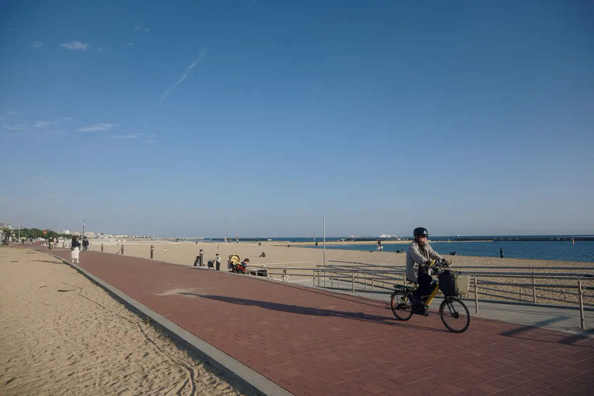 A cyclist rides a path beside a sandy beach and the ocean.