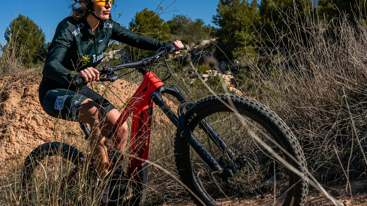 A person rides a bicycle with a battery on the frame along a coastal dirt path.