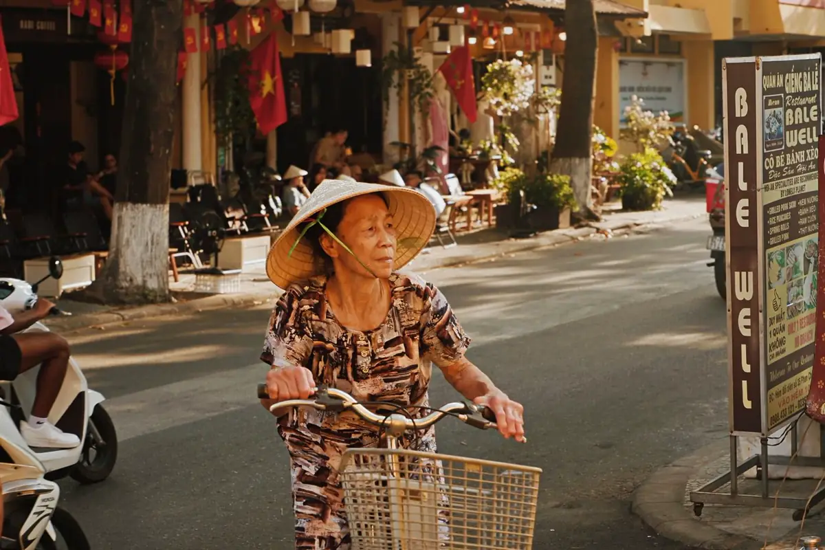 An older woman rides a bicycle along a sunny street.